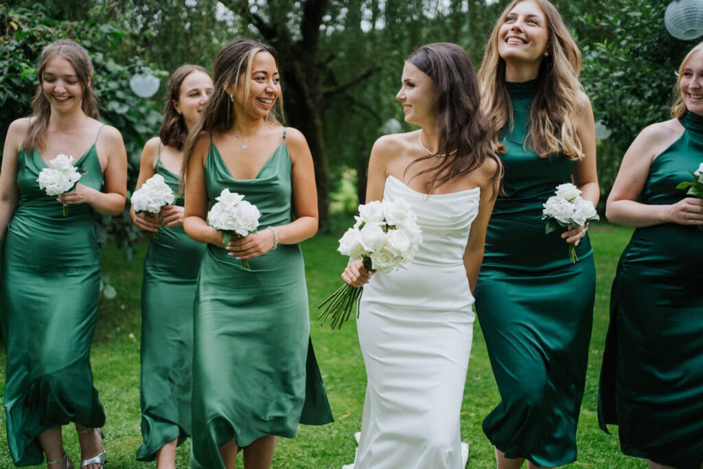Elegant bride and bridesmaids walking outdoors with white bouquets at wedding celebration.