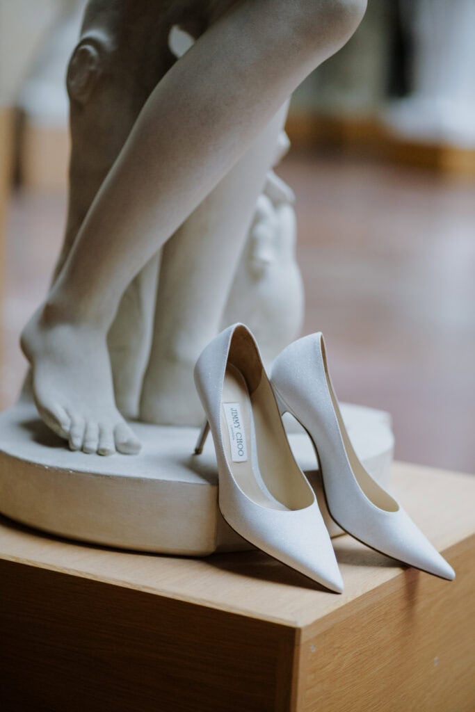 Elegant white Jimmy Choo high heels displayed next to a classical sculpture, highlighting artistry and fashion.