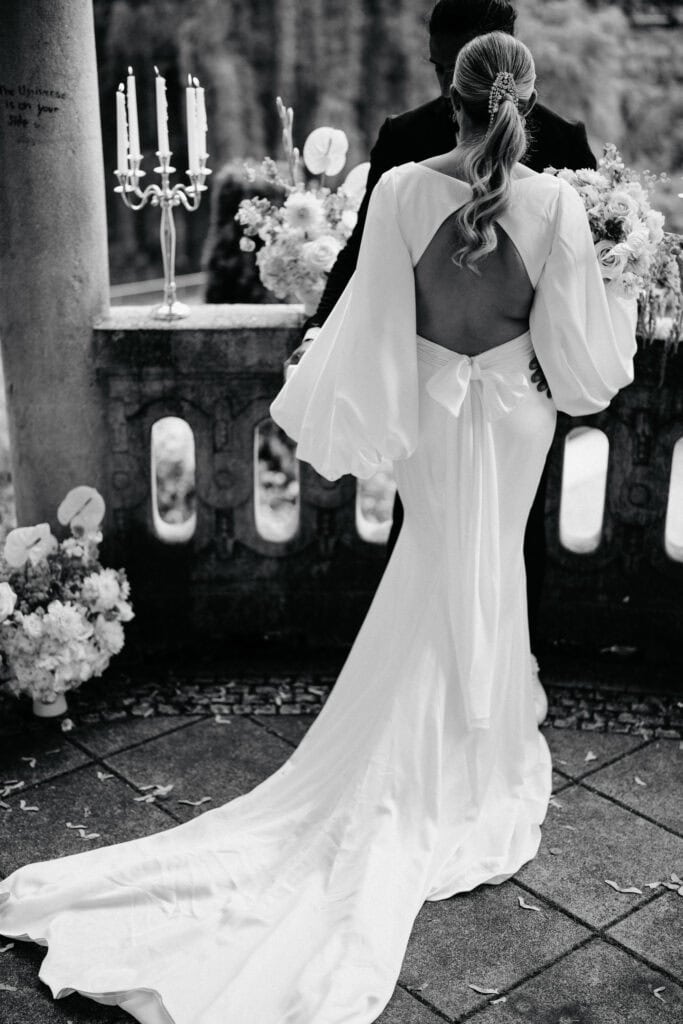 Elegant wedding bride in a flowing white gown with open back at outdoor ceremony.