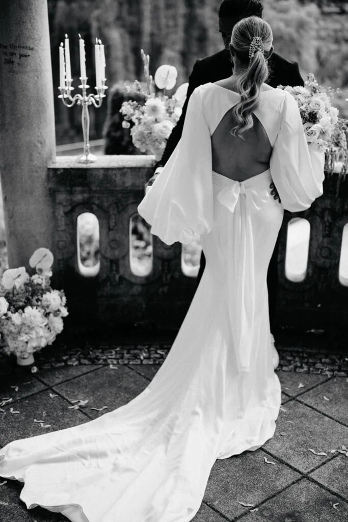 Elegant wedding bride in a flowing white gown with open back at outdoor ceremony.