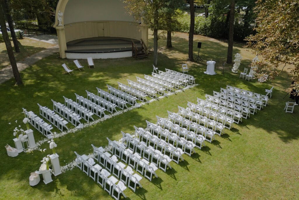White wedding chairs setup in outdoor garden with stage for a real life theatrical event.