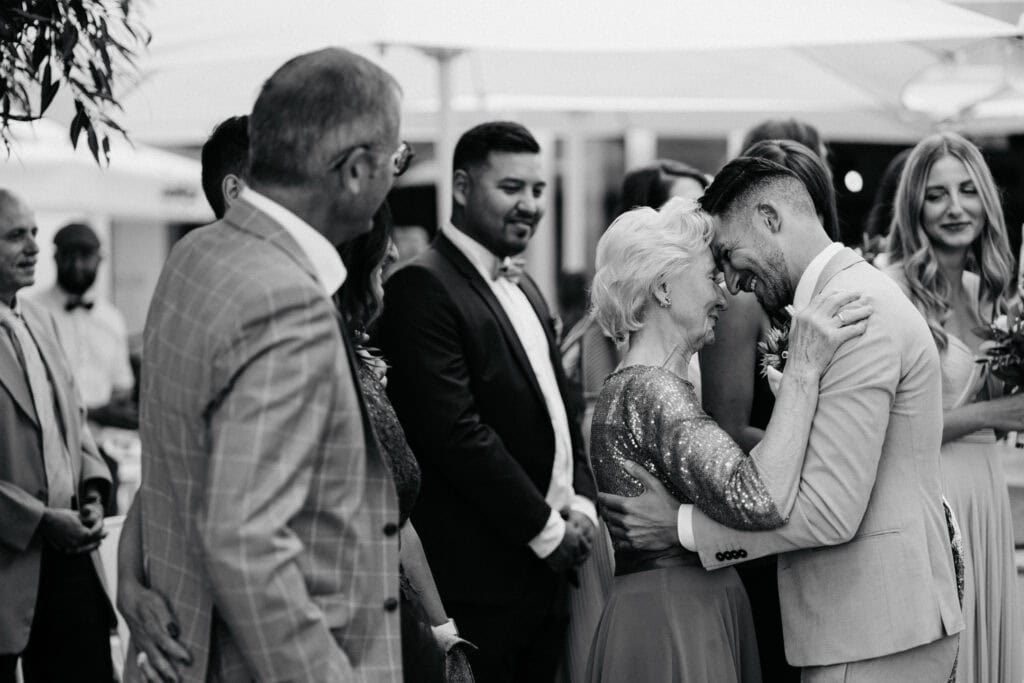 Happy groom and his grandmother sharing a joyful moment amid family and friends outdoors