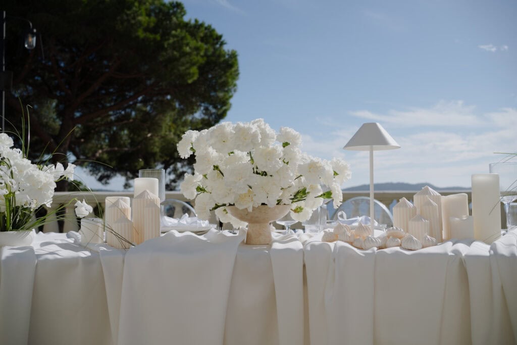 Elegante Hochzeitstafel im Freien, dekoriert mit weißen Blumen, Kerzen und modernen Akzenten unter einem klaren blauen Himmel.