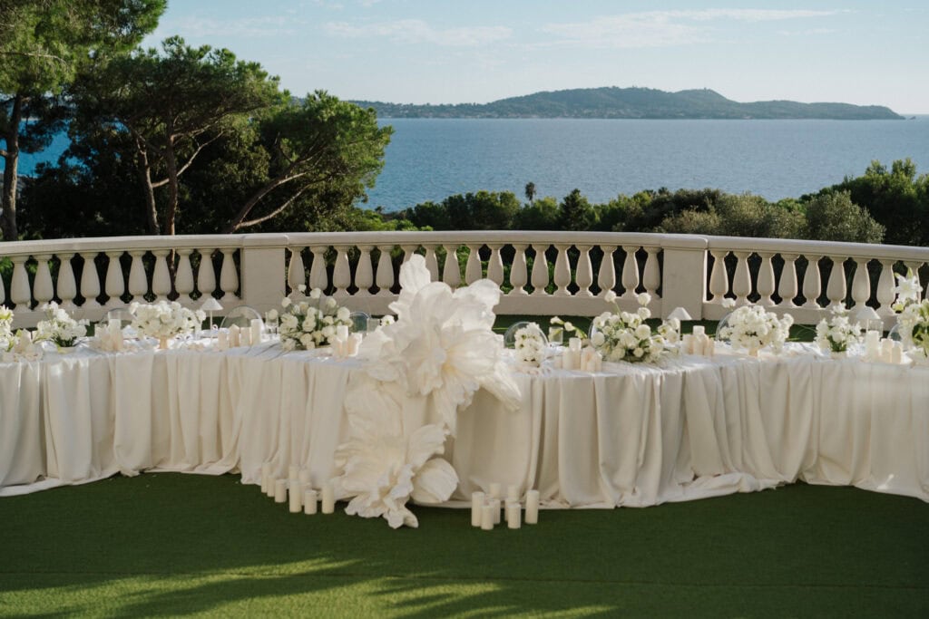 Eleganter Hochzeitsempfang im Freien mit weißen Blumenarrangements, Kerzen und einem malerischen Meerblick im Hintergrund.