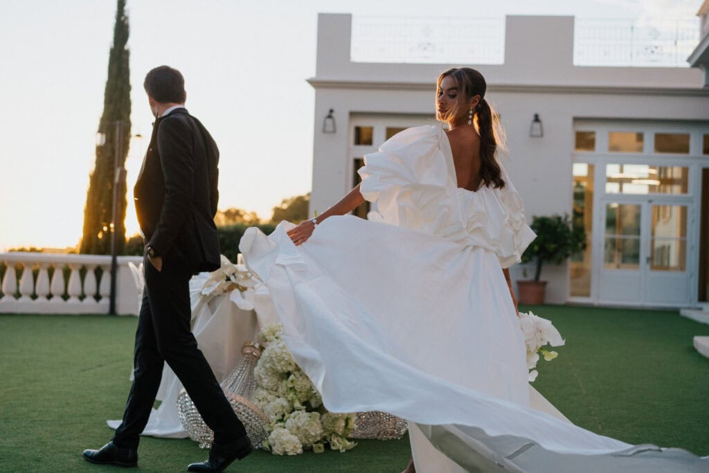 Die elegante Braut wirbelt in einem luxuriösen weißen Hochzeitskleid auf einer sonnigen Terrasse im Freien.