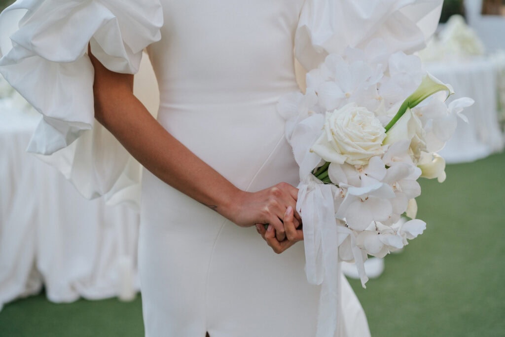 Elegante Braut mit einem weißen Blumenstrauß aus Rosen, Calla-Lilien und Orchideen, der einen raffinierten und romantischen Hochzeitsstil unterstreicht, fotografiert in Castel Bay.