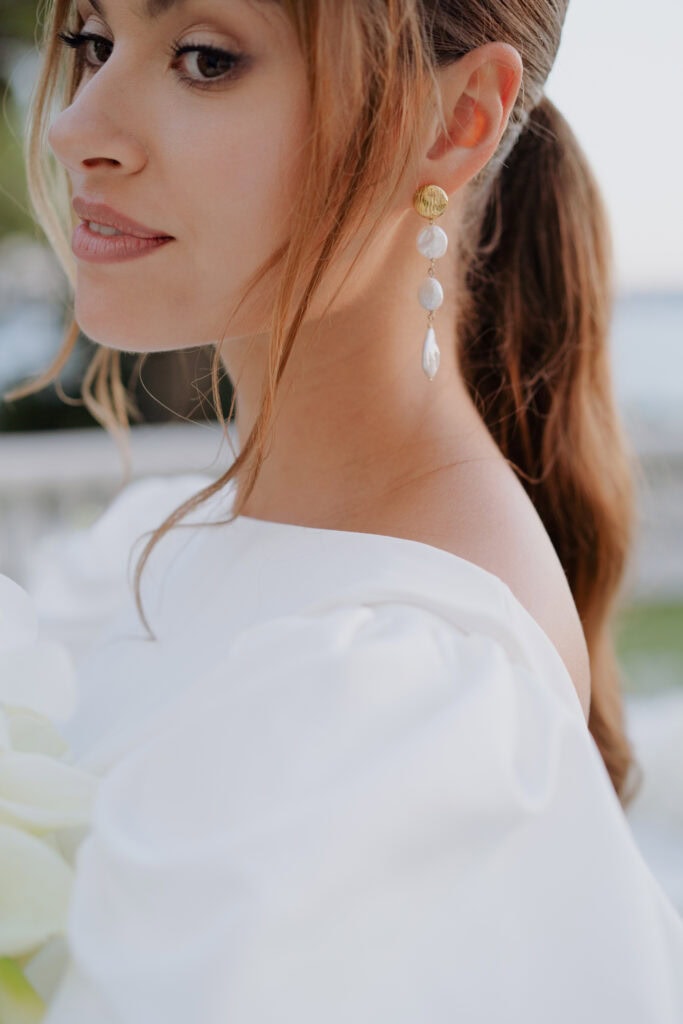 Elegante Braut in Castel Bay mit Perlen- und Goldohrringen, die Luxusschmuck und klassische Mode demonstrieren.