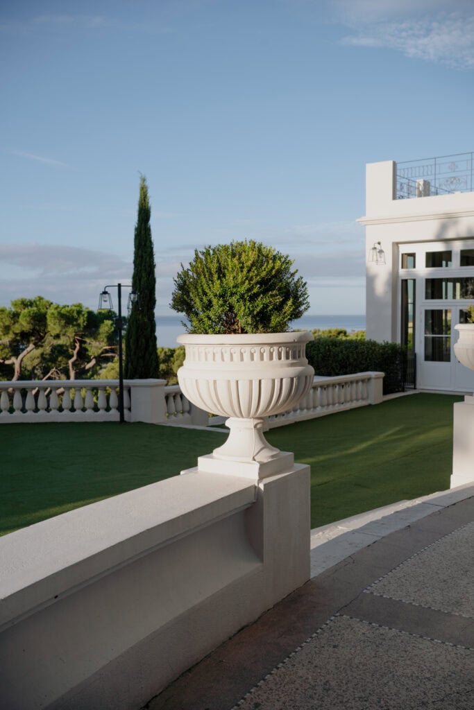 Elegante weiße Villa mit üppigem Grün und malerischem Meerblick im Hintergrund.