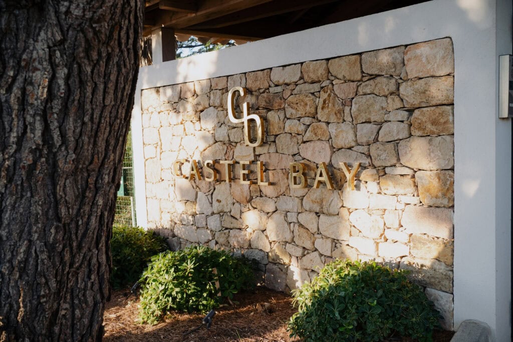 Elegantes Steinschild an der Castel Bay mit üppigem Grün und warmem Sonnenlicht, das professionelle Architekturfotografie an einem malerischen Ort am Wasser zeigt.
