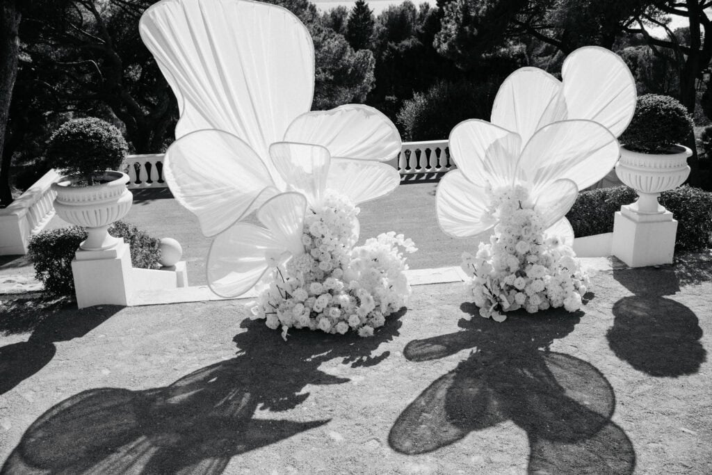 Elegante Hochzeitszeremonie im Freien mit weißen Blumenarrangements und malerischem Meerblick im Hintergrund.