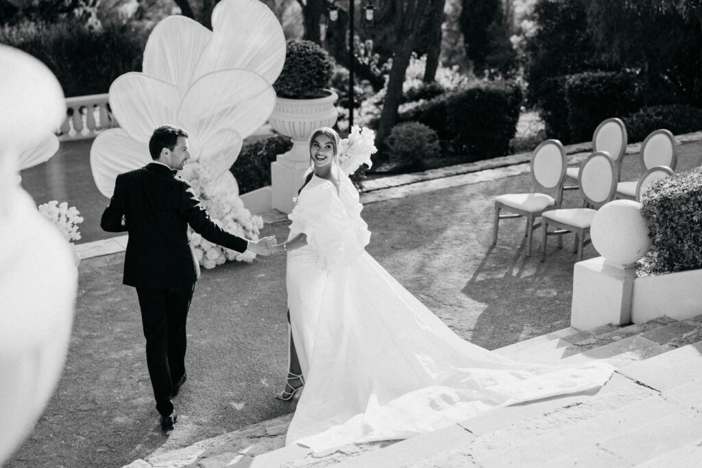 Elegante Braut und Bräutigam halten sich während einer Hochzeitszeremonie im Freien in einem üppigen Garten an den Händen.