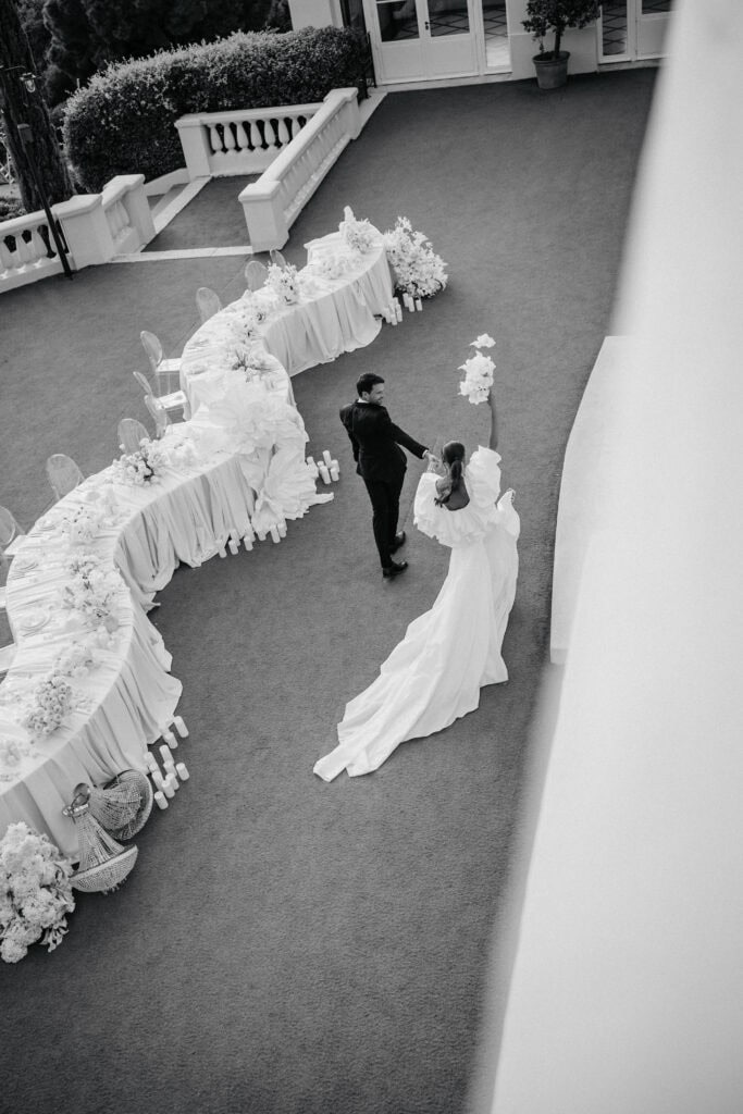 Eleganter Hochzeitsempfang mit Braut und Bräutigam in einem wunderschön dekorierten Raum mit einem langen, drapierten Tisch, der mit Blumenarrangements geschmückt ist. Die Braut hält einen Blumenstrauß in der Hand und tanzt mit dem Bräutigam, wobei sie einen romantischen Moment einfängt.
