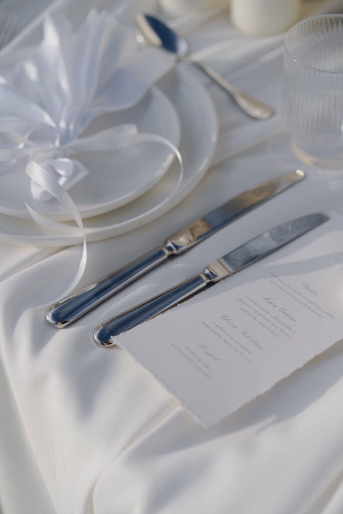 Elegant gedeckter Hochzeitstisch mit poliertem Silberbesteck, zarter Menükarte und raffinierten Gläsern.