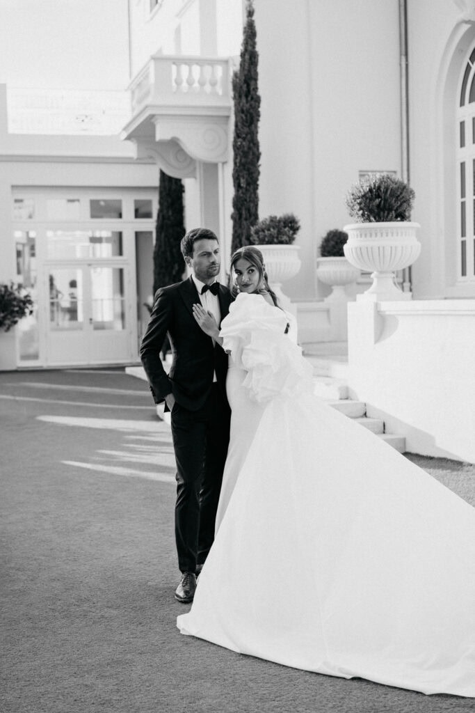 Elegantes Hochzeitspaar in stilvoller formeller Kleidung steht im Freien vor einem luxuriösen Gebäude in Castel Bay.