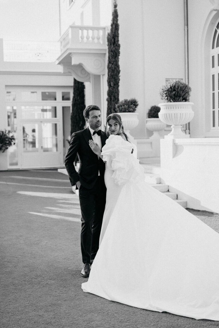 Elegantes Hochzeitspaar in stilvoller formeller Kleidung steht im Freien vor einem luxuriösen Gebäude in Castel Bay.