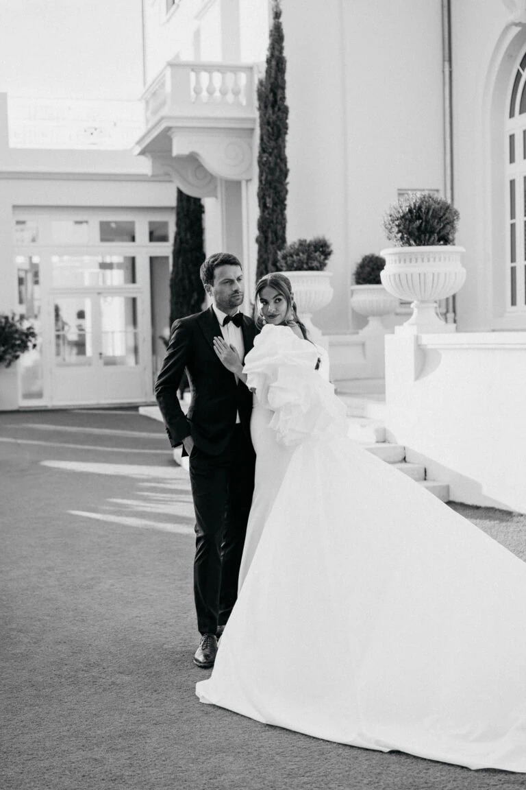 Elegant wedding couple in stylish formal attire standing outdoors in front of a luxurious building at Castel Bay.