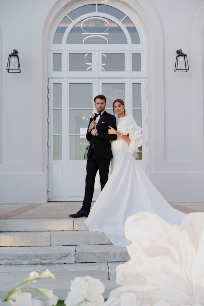 Elegantes Brautpaarporträt vor einer modernen Hochzeitslocation mit weißer Bogentür und moderner Beleuchtung.