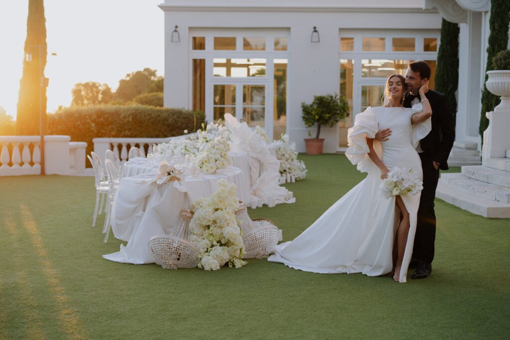 Ein elegantes Paar feiert seine Hochzeit im Freien bei Sonnenuntergang in einer luxuriösen Gartenanlage.